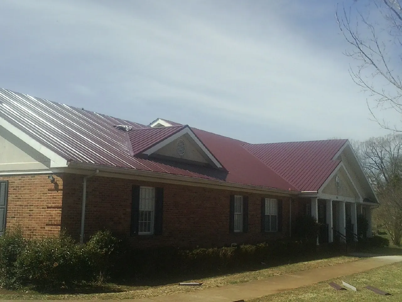 Red metal roof with gabled entries on a long brick building, from a Hail Damage Roof Repair job in Walton