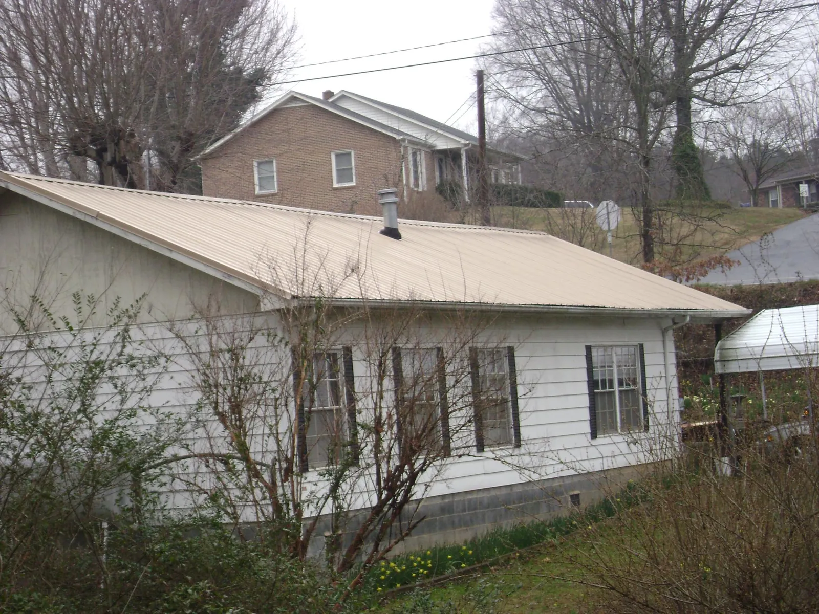 Tan metal roof on a white sided house set into a hillside — Commercial Roofing by Roofing Brothers in Walton