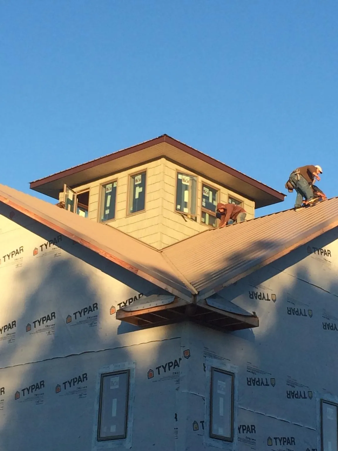 Roofers working around a rooftop cupola on a new metal roof at sunset in Walton